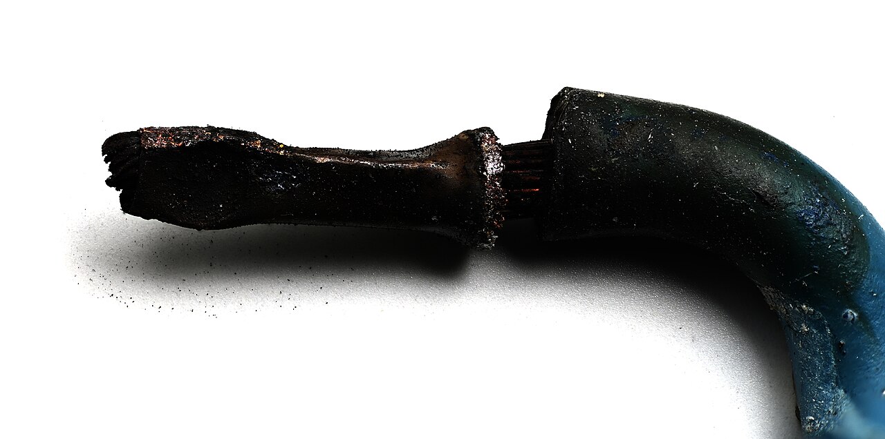 A crimped wire-end ferrule burnt black and deformed, with charred copper strands visible at the junction and the blue cable insulation scorched and blistered where it meets the joint.